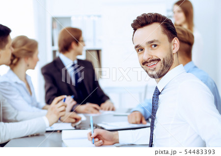 Businessman headshot against a group of business people at a meeting or negotiation in office Businessman headshot against a group of business people at a meeting or negotiation in office 54483393