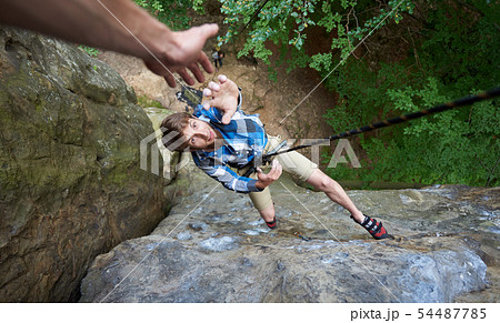Climber hanging on rope between rocks and stretching out his hand. Hand helping in the rock climbing Climber hanging on rope between rocks and stretching out his hand. Hand helping in the rock climbing 54487785