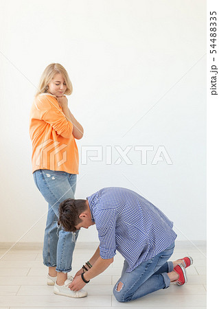 Young man tying shoelaces of his beloved woman posing on the white background. Concept of courtship 54488335