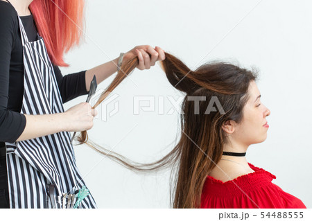 Hair Stylist, coloring and people concept - red hair hairdresser coloring young woman in red shirt Hair Stylist, coloring and people concept - red hair hairdresser coloring young woman in red shirt 54488555