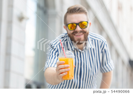 Portrait of a blurred stylish young hipster male with beard and mustache holding fresh orange juice 54490066
