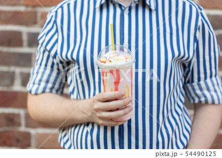 An unidentified young man in a shirt holds in his hands a jar of fruit milk shake standing against a 54490125