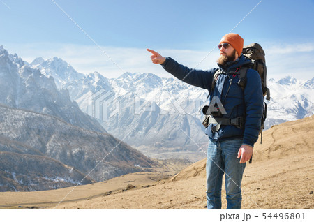 Bearded man in sunglasses and a hat with a backpack points hand at the mountains. Travel concept on 54496801