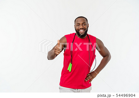 Shot of masculine man skipping rope. Muscular young man exercising with jumping rope against grey 54496904