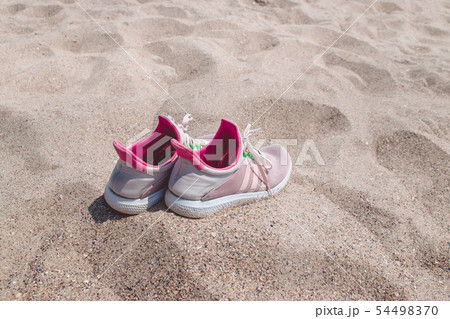 Concept with pink sneakers on bright sea sand. Concept with pink sneakers on bright sea sand. 54498370