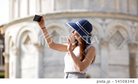 Young attractive woman stand under Pisa tower take a selfie and waving with her hand Young attractive woman stand under Pisa tower take a selfie and waving with her hand 54508348