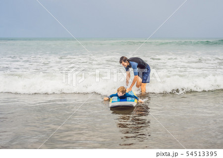 Father or instructor teaching his 5 year old son how to surf in the sea on vacation or holiday 54513395