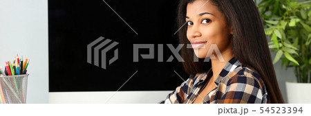 Black smiling woman sitting at workplace looking at camera Black smiling woman sitting at workplace looking at camera 54523394