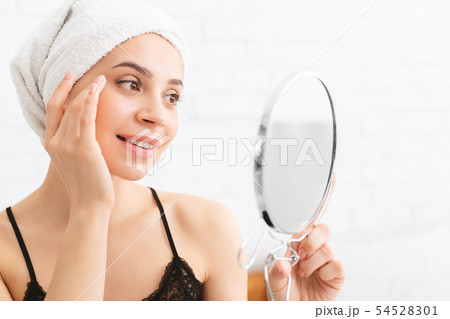 Millennial woman looking at mirror, wearing towel on head after shower 54528301