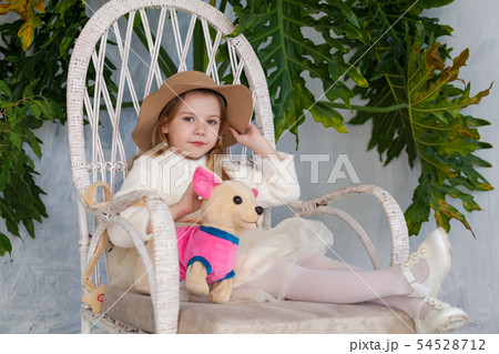 Little beautiful girl in big hat sits in a white chair 54528712