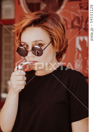 Millennial girl with short red hair and mirror sunglasses smoking cigarette 54531126