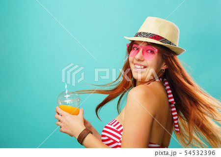 Woman wearing swimsuit and hat drinks fruit juice from a cup 54532396