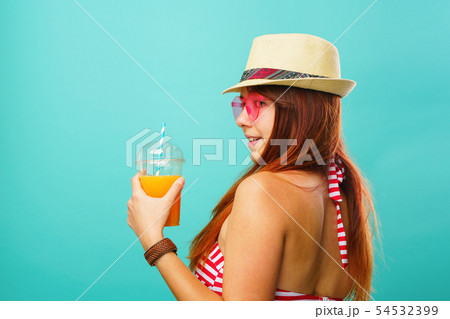 Woman wearing swimsuit and hat drinks fruit juice from a cup 54532399