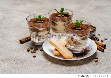 Classic tiramisu dessert in a glass cup and savoiardi cookies on plate on concrete background Classic tiramisu dessert in a glass cup and savoiardi cookies on plate on concrete background 54545561