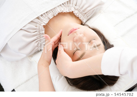 フェイスマッサージを受ける女性と施術者の手元 54545702