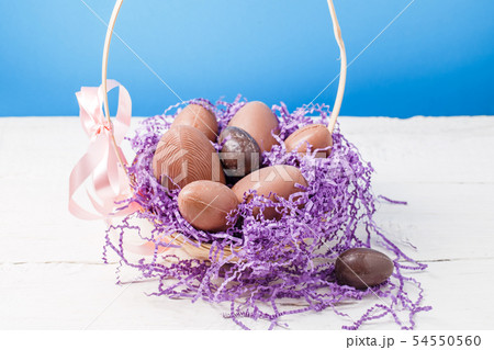 Photo of chicken , chocolate eggs, purple decorative paper in basket 54550560