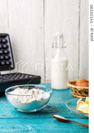 Making waffles at home - waffle iron and ingredients - milk, eggs and flour. Making waffles at home - waffle iron and ingredients - milk, eggs and flour. 54550590