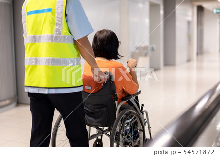 Caretaker push elderly woman on wheelchair in airport terminal. Caretaker push elderly woman on wheelchair in airport terminal. 54571872