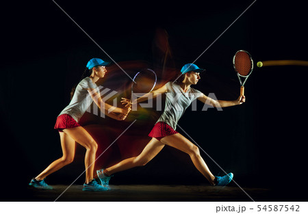 One caucasian woman playing tennis on black background in mixed light 54587542