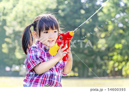 新緑の樹木を背景に水鉄砲で遊ぶ幼い女の子。自由、遊び、子供、幸せ、元気イメージ 54600393