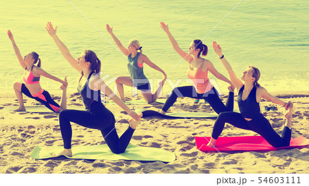 Group of sporty girls practicing various yoga positions during training on beach Group of sporty girls practicing various yoga positions during training on beach 54603111