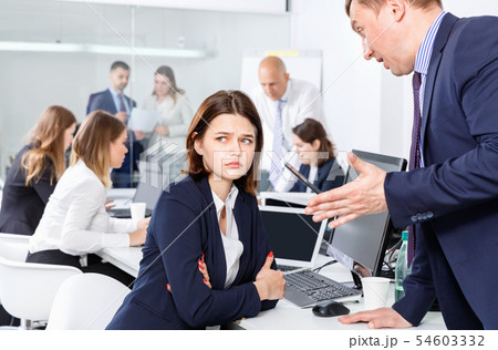 Outraged manager expressing dissatisfaction with work of frustrated young woman in modern office Outraged manager expressing dissatisfaction with work of frustrated young woman in modern office 54603332
