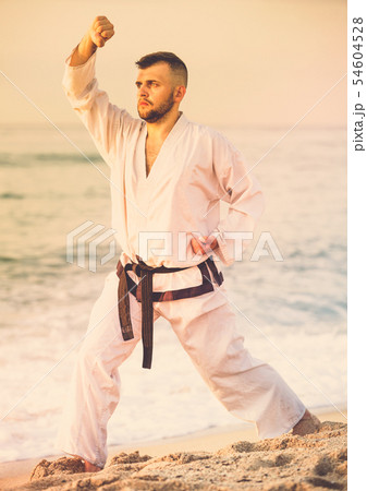 Guy doing karate poses at sunset sea shore 54604528