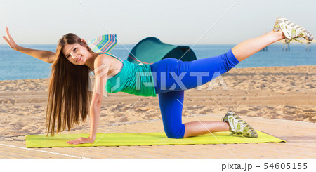 Woman in blue T-shirt is practicing stretching on the beach. 54605155