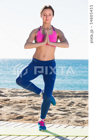 Sportswoman practices asanas of yoga on beach Sportswoman practices asanas of yoga on beach 54605455