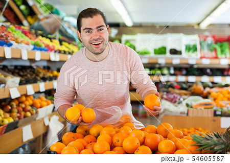 Young male looking fresh oranges in fruit store indoor Young male looking fresh oranges in fruit store indoor 54605587