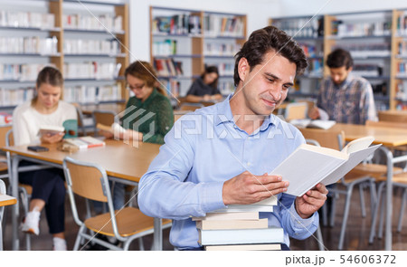 Smiling man reading book in library 54606372