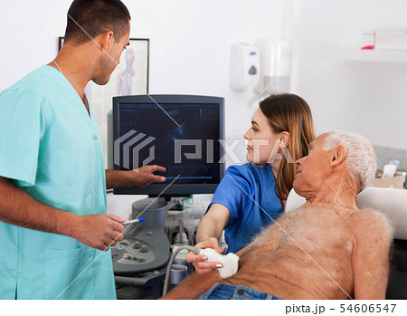 Two confident sonographers working together examining patient wi Two confident sonographers working together examining patient wi 54606547