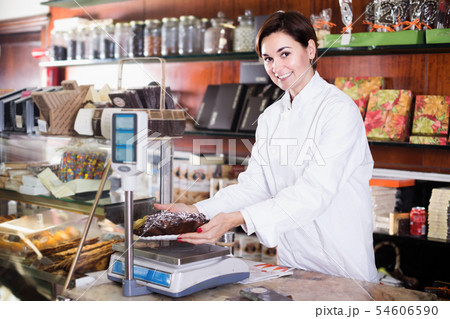 Smiling female seller weighing festive chocolate cake Smiling female seller weighing festive chocolate cake 54606590