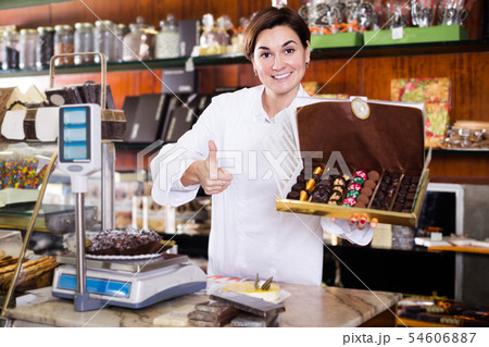Positive female seller showing box of chocolate sweets 54606887
