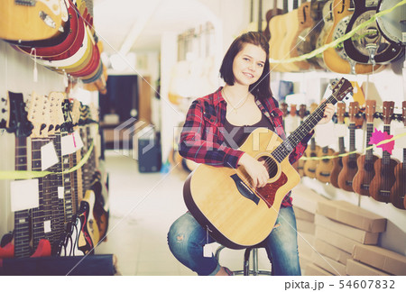 Nice girl examining various acoustic guitars Nice girl examining various acoustic guitars 54607832