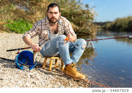 Bearded adult man posing with fish near river in summertime 54607929