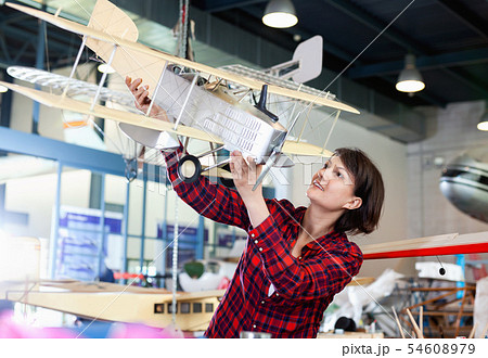 Smiling woman showing sports biplane model she created in aircraft workshop Smiling woman showing sports biplane model she created in aircraft workshop 54608979