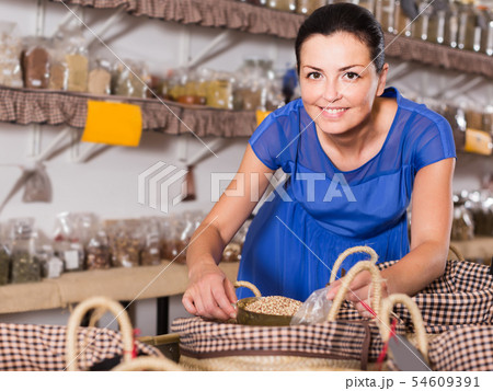 woman taking dried beans with shovel from backet in organic shop 54609391