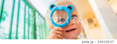 Boy looking in a magnifying glass against the background of the garden. Home schooling BANNER, LONG 54619237