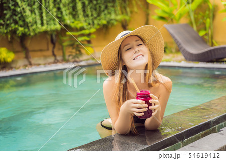 Young woman drinking Dragon fruit smoothies on the background of the pool. Fruit smoothie - healthy Young woman drinking Dragon fruit smoothies on the background of the pool. Fruit smoothie - healthy 54619412