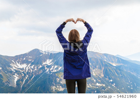 Young woman making heart shape with hands, enjoying the view of green hills mountains. 54621960
