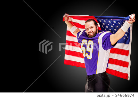 Patriotic american football player posing at camera on black background with usa flag. The concept Patriotic american football player posing at camera on black background with usa flag. The concept 54666974