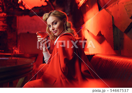Image of happy blonde woman in red jacket looking at camera with cocktail in her hand in nightclub Image of happy blonde woman in red jacket looking at camera with cocktail in her hand in nightclub 54667537