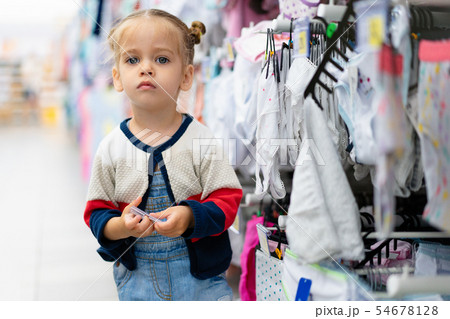 A little Caucasian girl is standing near a shop A little Caucasian girl is standing near a shop 54678128
