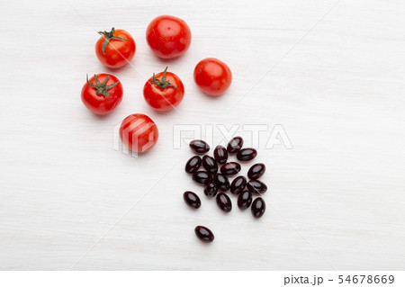 Tomatoes lie on a white table next to vitamins in the form of jelly on a white table. Concept of Tomatoes lie on a white table next to vitamins in the form of jelly on a white table. Concept of 54678669