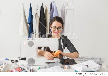 people, fashion and showroom concept - young fashion designer sews clothes on a sewing machine people, fashion and showroom concept - young fashion designer sews clothes on a sewing machine 54678745