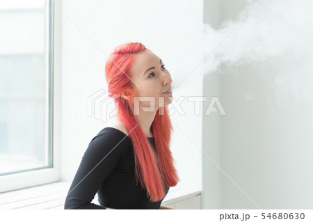 Vape, addiction and people concept - woman with red hair is smoking vape Vape, addiction and people concept - woman with red hair is smoking vape 54680630