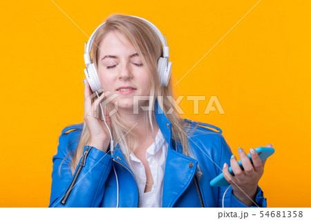 Portrait of cute positive young blonde girl listening to favorite music in headphones in blue 54681358