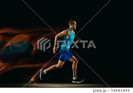 Professional male runner training isolated on black studio background in mixed light Professional male runner training isolated on black studio background in mixed light 54691944