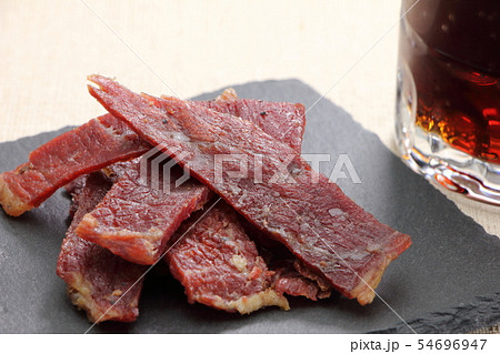 スレートプレートにのせられたおつまみ、ビーフジャーキー。奥にはコークハイの入ったジョッキ。 54696947